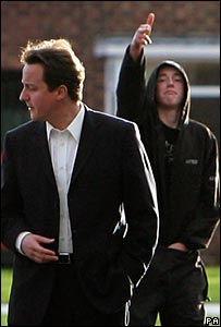 David Cameron and hoodie kid making a gun from his hand in the background